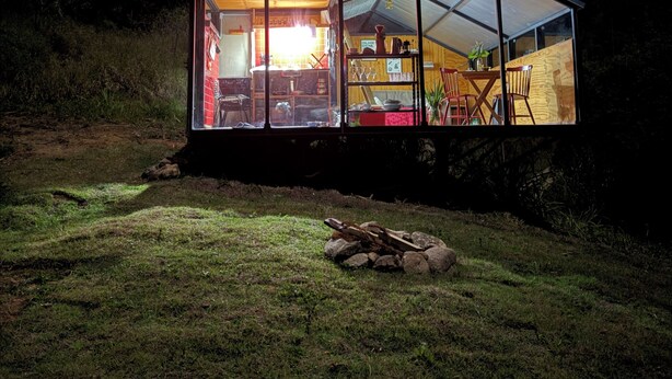 A modern glass house with a triangular roof, a visible kitchen area, and a dining space. - Araucaria Cabin: Design and Nature (Itajubá)