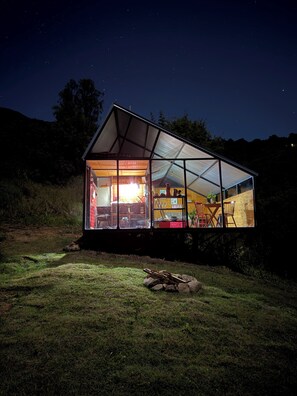 Une maison moderne en verre, dotée d’un toit triangulaire, d’une cuisine ouverte et d’un espace repas.