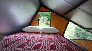 A small, triangular room with a bed, two pillows, and a window. - Araucaria Cabin: Design and Nature (Itajubá)