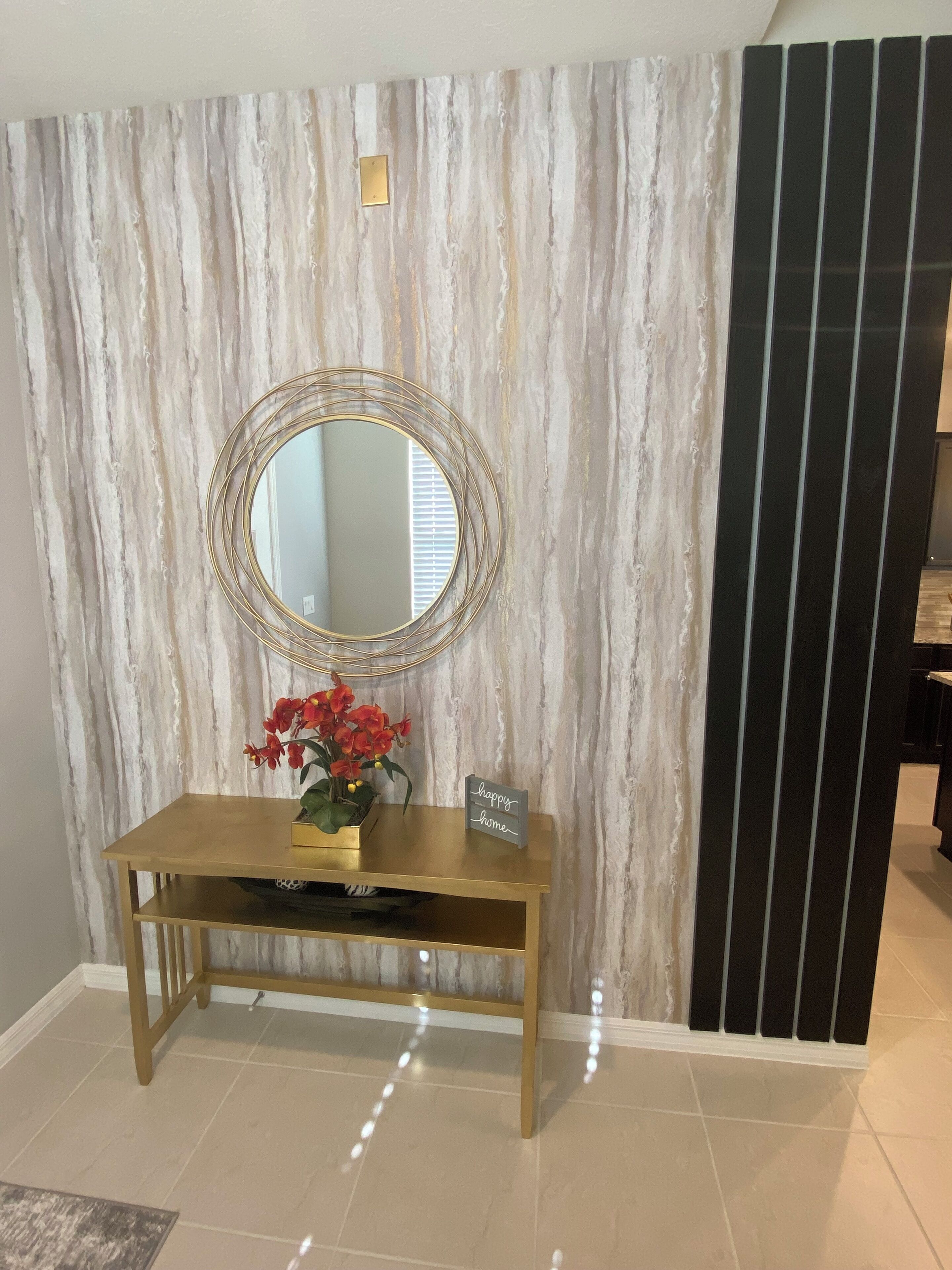 A reception area with a marble-patterned wall, a round mirror, a gold console table, a potted red orchid, and a 'happy home' sign.