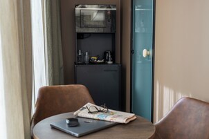 Una piccola cucina compatta con forno a microonde, frigorifero e macchina da caffè. Su un tavolo, un laptop e un paio di occhiali.