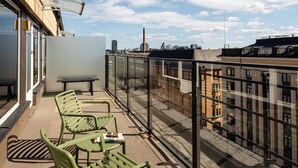 A balcony with green chairs and a table, overlooking a cityscape with buildings and a smokestack. - Hotel H28 (Tampere)