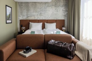 A hotel room with a bed, a brown sofa, a brown leather bag, and a framed picture on the wall. - Hotel H28 (Tampere)