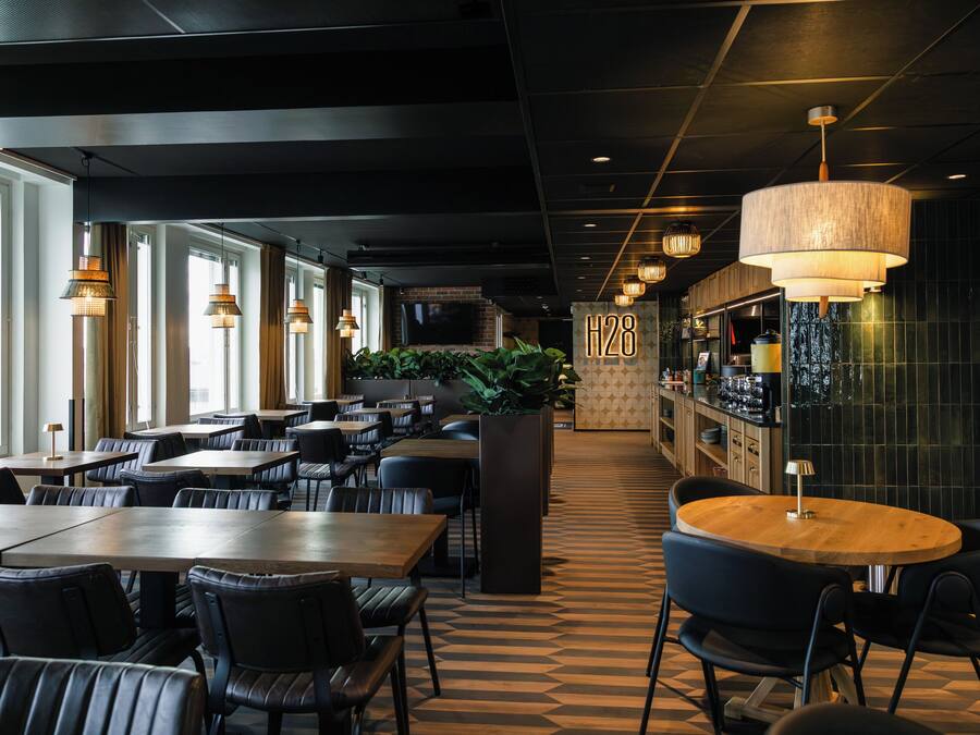 A modern restaurant interior with multiple dining tables and chairs, a large potted plant, and a bar area.