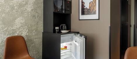 A compact kitchenette with a refrigerator, a coffee maker, and a bowl on the counter.