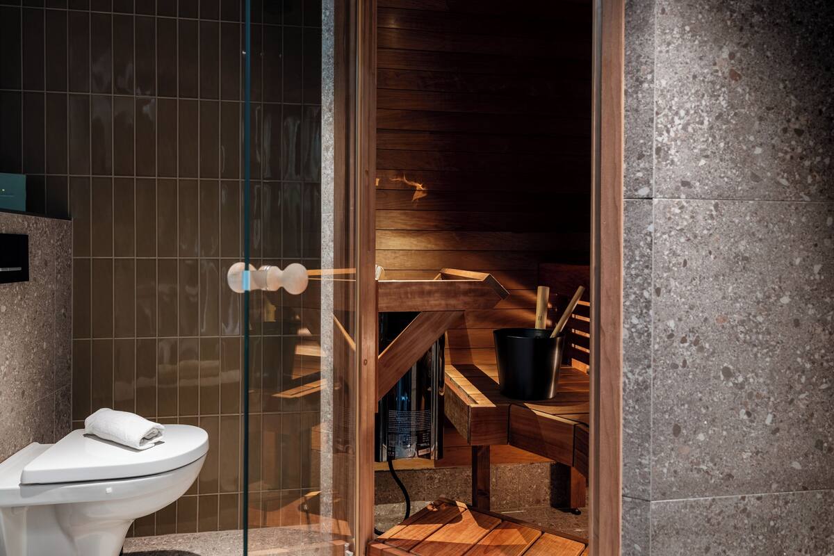 A modern bathroom with a glass shower enclosure, a wooden bench, and a toilet.