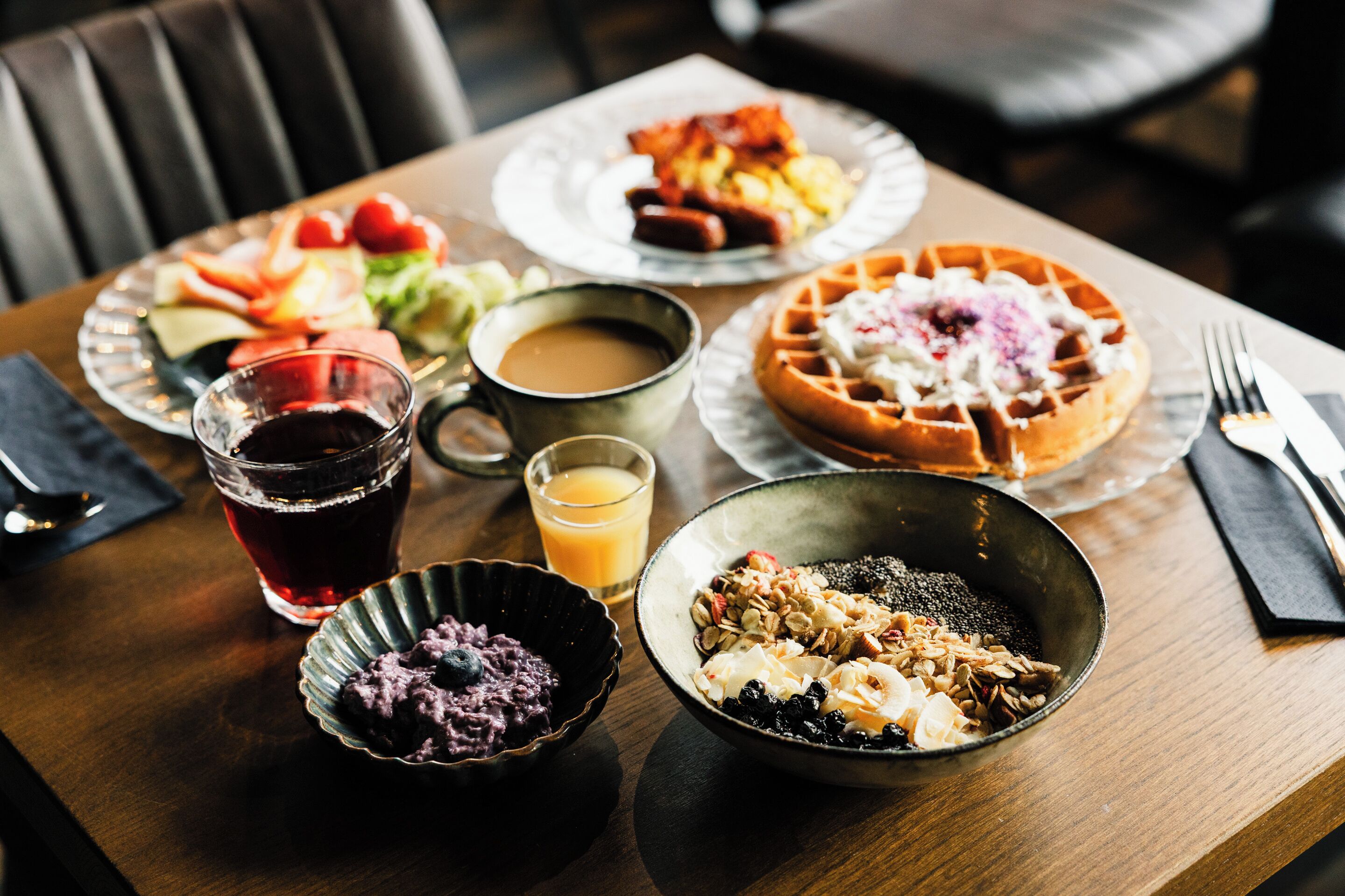 Una mesa de desayuno con diversos platos, como waffles, panqueques y un tazón de cereales.