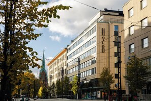 A multi-story building with a modern architectural style, featuring large windows and a visible church spire in the background. - Hotel H28 (Tampere)
