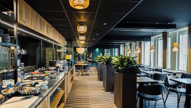 A modern restaurant with a long counter, multiple seating areas, and large windows. - Hotel H28 (Tampere)