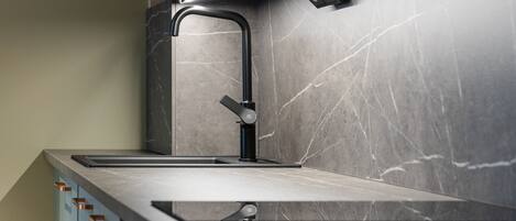 A modern kitchen with a sleek faucet, a countertop, and a backsplash with a marble-like pattern.