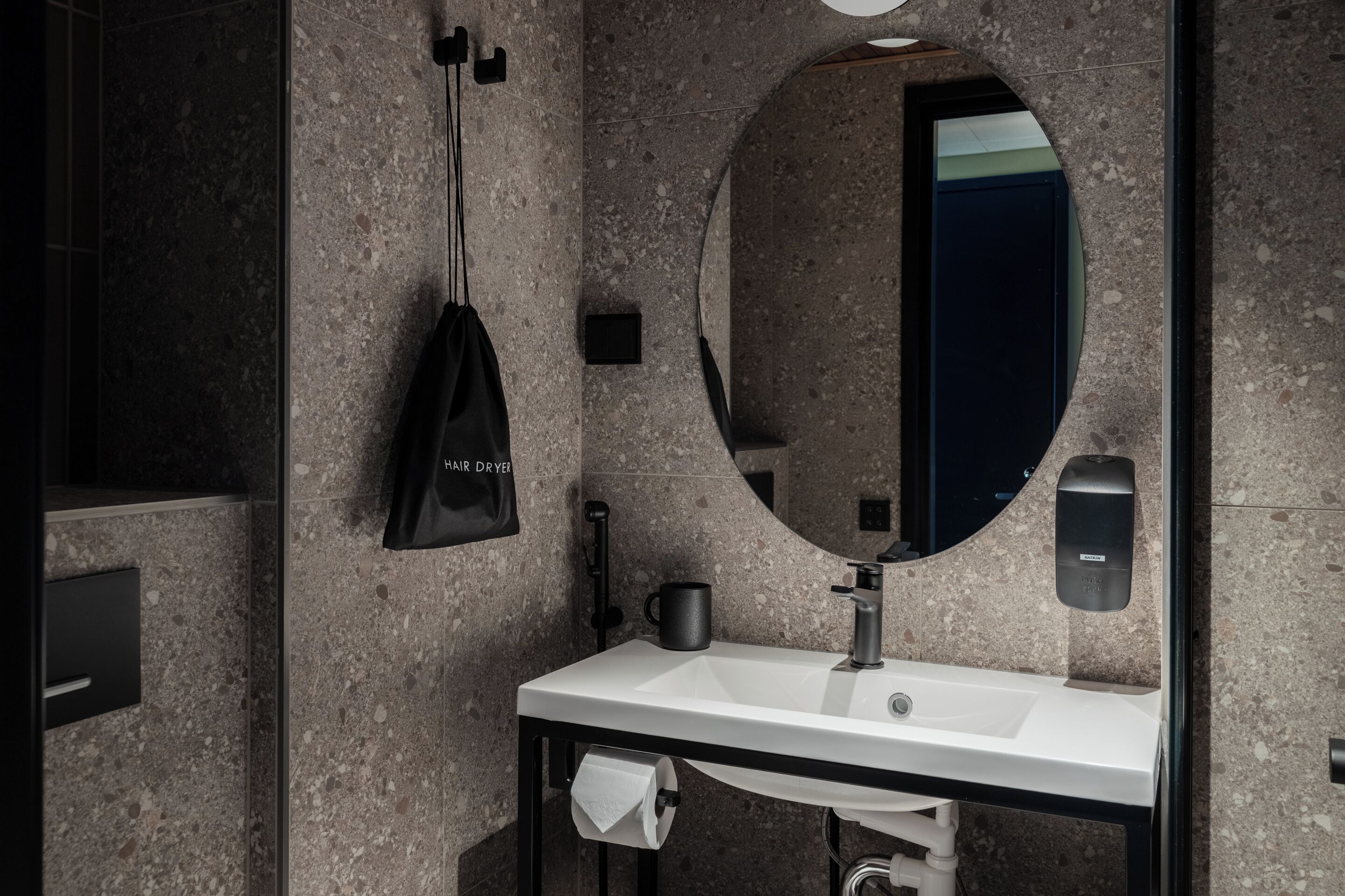 A modern bathroom with a granite countertop sink, a large mirror, a hair dryer, and a soap dispenser.