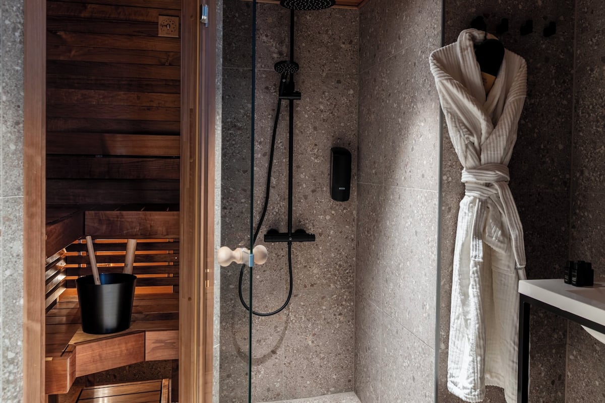 A modern bathroom with a wooden bench, a shower with a handheld showerhead, and a towel rack.