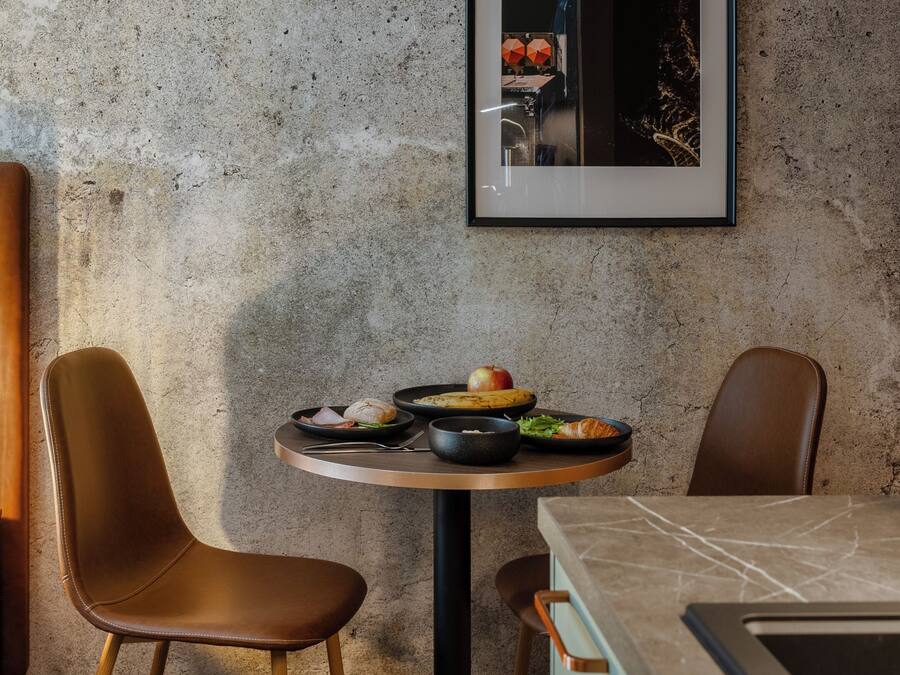 Un comedor moderno con una mesa redonda, dos sillas de cuero, un cuadro en la pared y una encimera de cocina con cajones.