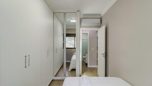 Ein Schlafzimmer mit Bett, Kleiderschrank und einem durchgegangenen Türbogen sichtbarem Badezimmer.