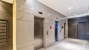 Un espace moderne pour les ascenseurs, doté d’un écran numérique, de boutons d’urgence et d’un panneau d’affichage fixé au mur.