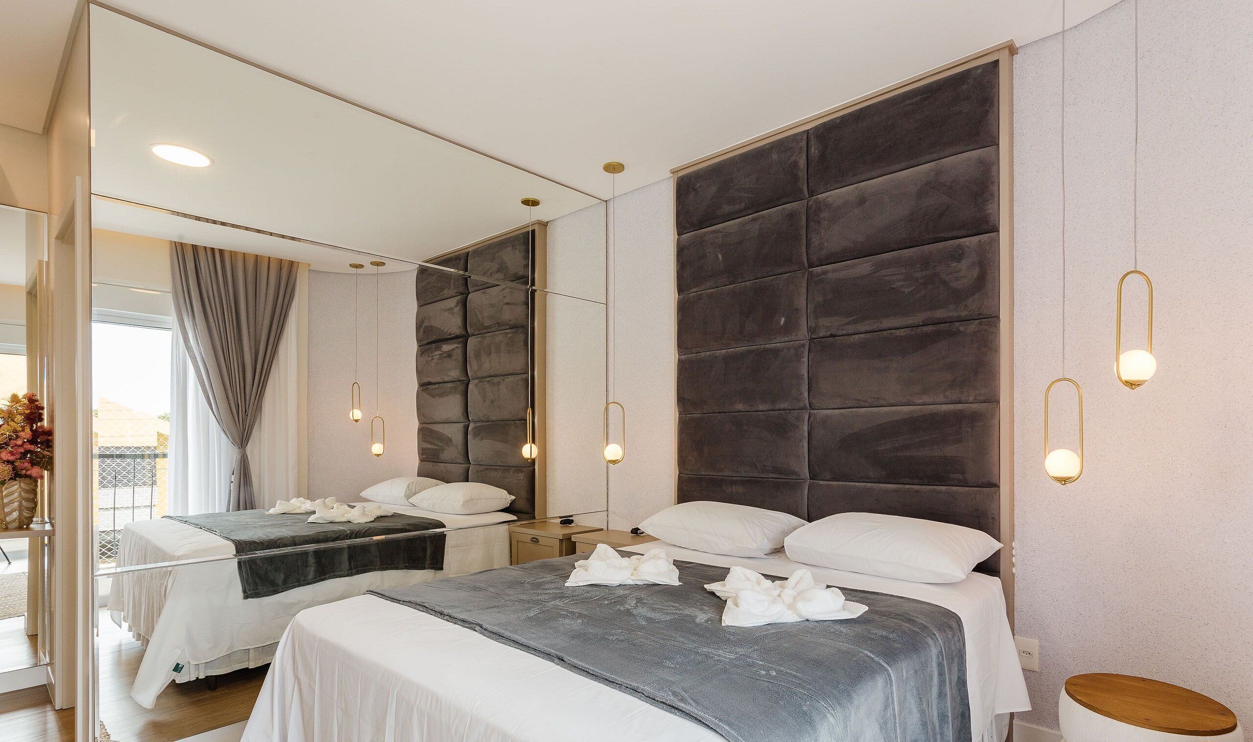 A modern hotel room with two beds, a large padded headboard, and pendant lighting.