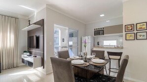 A modern kitchen with white cabinets, a built-in oven, and a microwave. There is a dining area with a table set for four, chairs, and a vase with flowers. - 2 Bedroooms Apt w/ BBQ 500m From the Beach Pts0101 (Florianópolis)