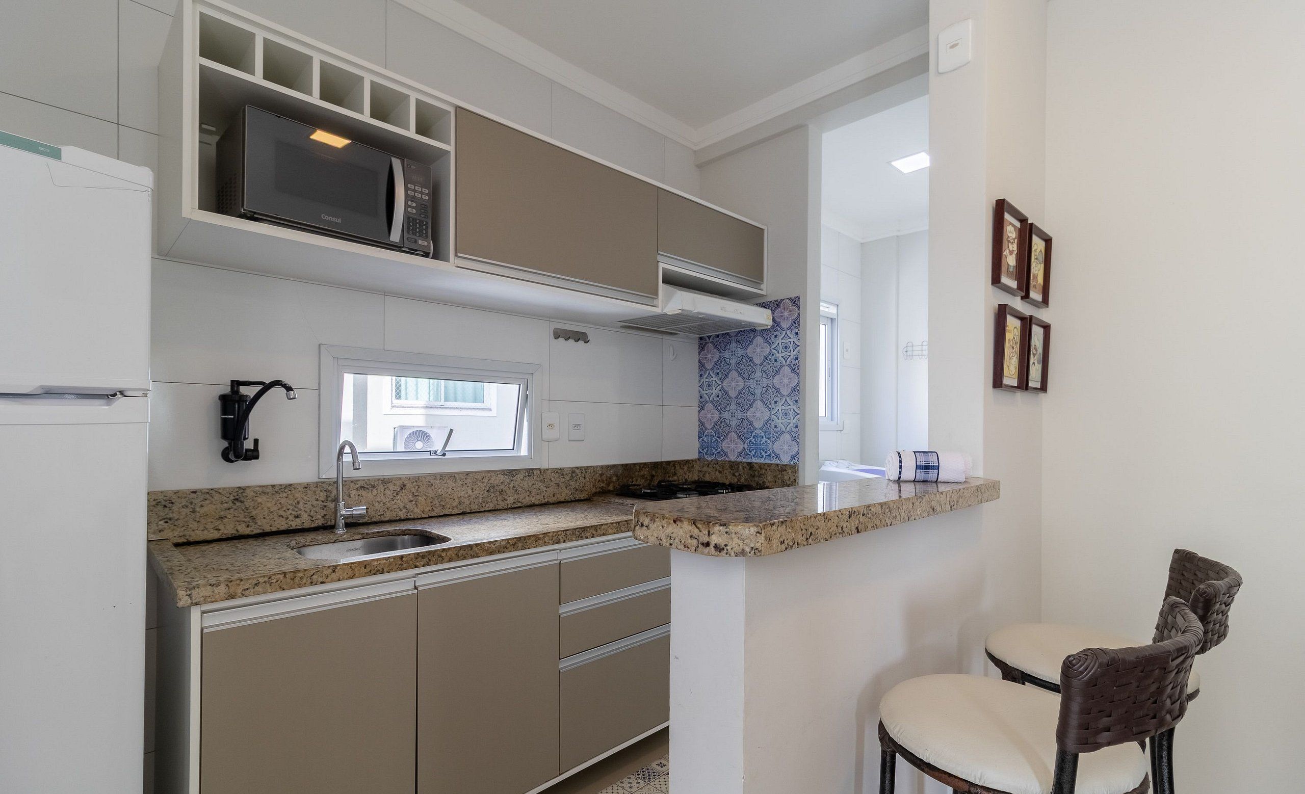A compact kitchen with a built-in microwave, a sink, and a small bar area with two chairs.
