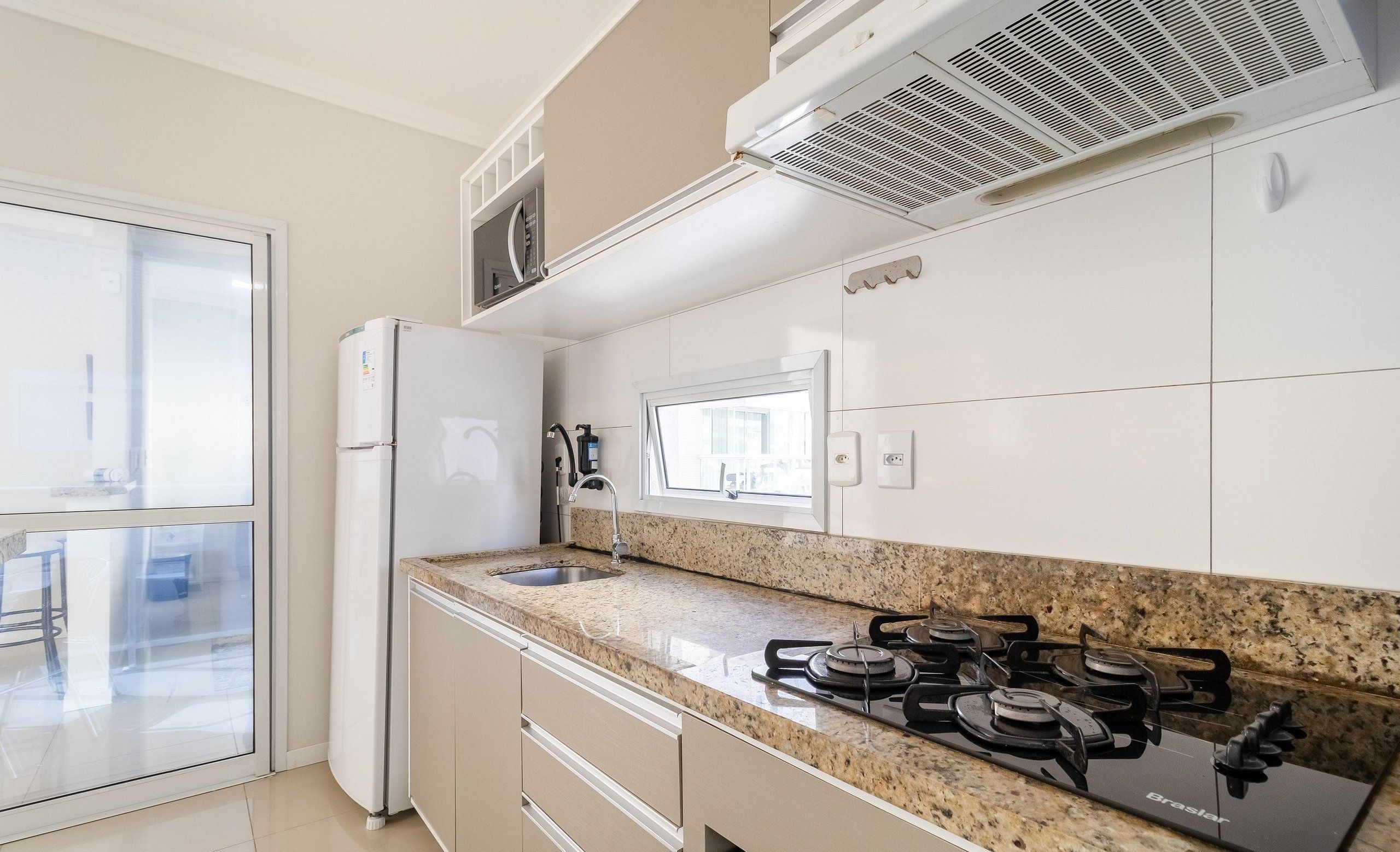 A modern kitchen with a gas stove, a refrigerator, and a window.
