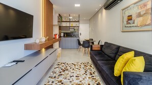A modern living room with a black sofa, a coffee table, and a TV. There is a kitchen area in the background with a dining table and chairs. - Charming Apartment 210m From Jurere Beach Psj0304 (Florianópolis)