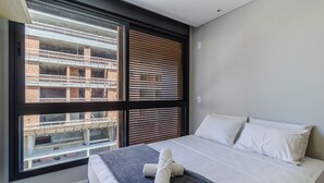 A modern bedroom with a large window, a bed with white linens, and a rolled towel on the bed. - Charming Apartment 210m From Jurere Beach Psj0304 (Florianópolis)