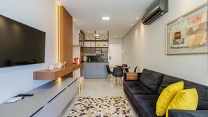 A modern living room with a black sofa, a coffee table, and a TV. There is a kitchen area in the background with a dining table and chairs. - Charming Apartment 210m From Jurere Beach Psj0304 (Florianópolis)