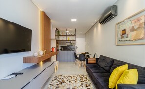 A modern living room with a black sofa, a coffee table, and a TV. There is a kitchen area in the background with a dining table and chairs. - Charming Apartment 210m From Jurere Beach Psj0304 (Florianópolis)