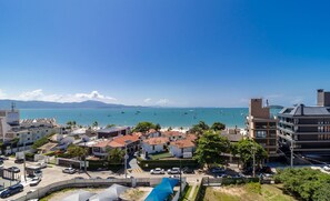 A coastal town with a view of the sea, featuring a hotel with a swimming pool, surrounded by residential buildings and parked cars. - Balcony With sea View 230m From the Beach! Prb0405 (Florianópolis)