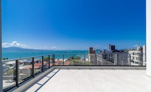 Un balcone con vista libera sul mare e sulle barche, con ringhiera in vetro e pavimento piastrellato.