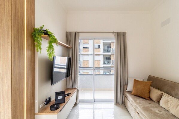 Una sala de estar moderna con un televisor de pantalla plana, una mesa consola de madera, un sofá y un balcón con cortinas.