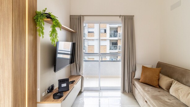 Een moderne woonkamer met een flatscreen televisie, een houten console, een bank en een balkon met gordijnen.