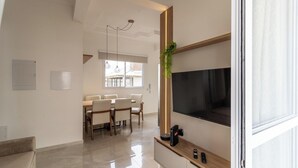 Een moderne woonkamer met een grote televisie, een houten dressoir en een eethoek met een tafel en stoelen.