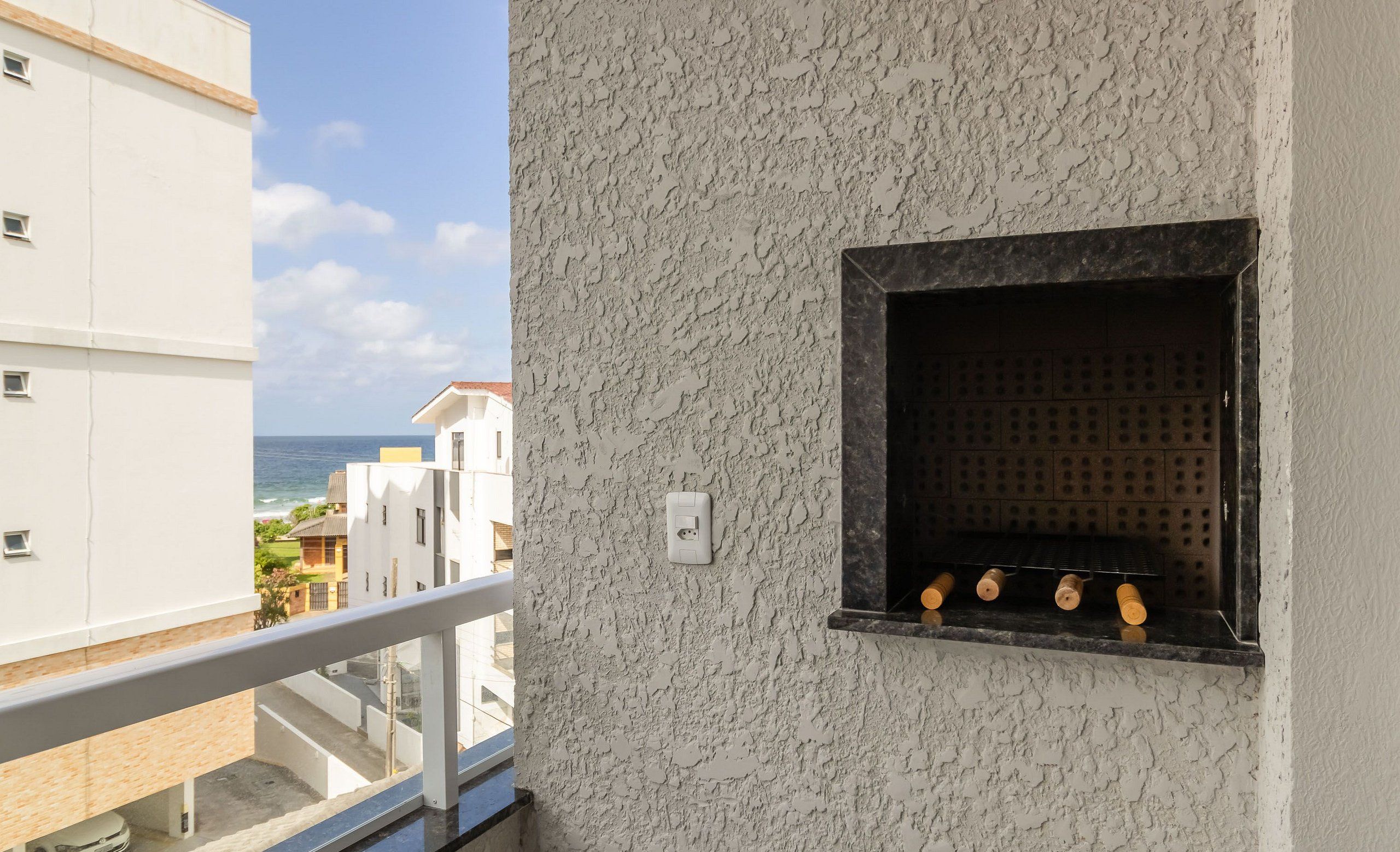 Ein Balkon mit Blick auf das Meer, eine strukturierte Wand und eine kleine Ablagefläche mit Gegenständen.