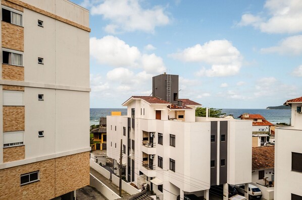 A multi-story building with balconies, a visible sea view, and a clear sky.