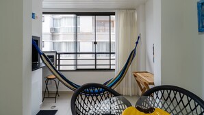 A room with a hammock, a small wooden table, a black chair, and a view of a balcony with white railings. - Apartment w/ Barbecue 450m From the Beach Pnm0202 (Florianópolis)