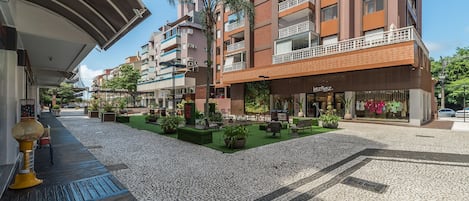 Un edificio moderno con varios balcones, un patio central con plantas y una tienda con un letrero visible.