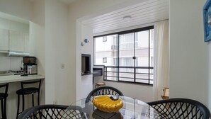 A compact kitchen with a gas stove, a coffee maker, and a dining area with a glass table and black chairs. - Apartment w/ Barbecue 450m From the Beach Pnm0202 (Florianópolis)