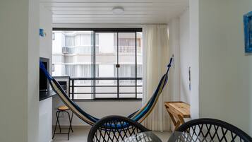 Una habitación con una hamaca, una pequeña mesa de madera, una silla negra y vistas a un balcón con barandillas blancas.