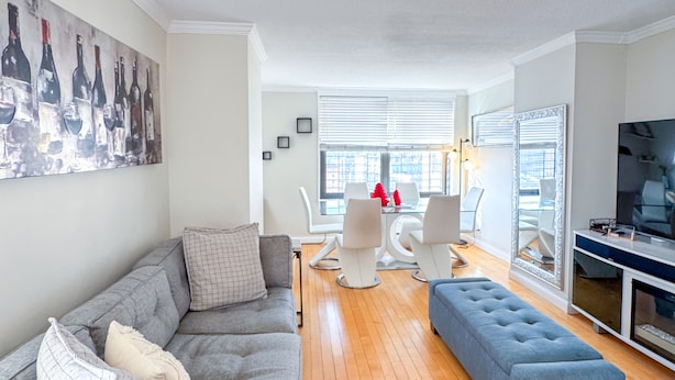 A modern living room with a grey sofa, a blue ottoman, and a dining area with white chairs and a table. - Columbia University 3Bedroom 1 1/2 Bath Across Cathedral of St. John the Divine (New York)