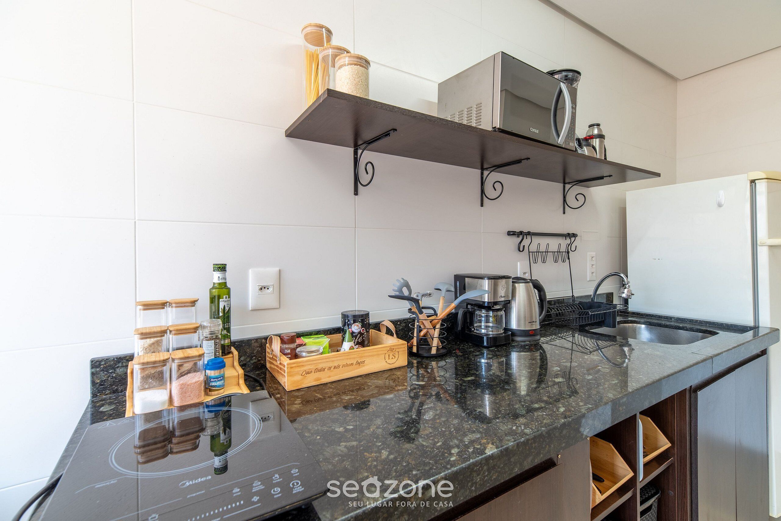 Una cocina moderna con encimera negra, placa de inducción integrada y electrodomésticos de acero inoxidable. Hay contenedores de madera para guardar cosas en la encimera y una cafetera.