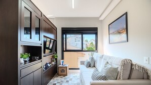 A modern living room with a sofa, a TV, and a view of buildings outside. - Charming Studio Just 200m From the Beach - Pmo0404 (Florianópolis)