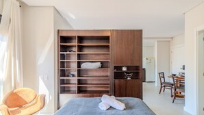 A bedroom with a large wardrobe, a bed with a grey blanket, a wooden chair, and a dining area with a table and chairs. - Charming Studio Just 200m From the Beach - Pmo0404 (Florianópolis)