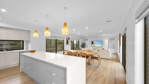 A modern kitchen with a large island, wooden dining table, and a cozy living area with a TV and artwork.