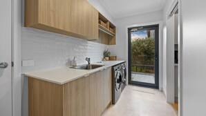 A modern kitchen with wooden cabinets, a white tiled backsplash, a stainless steel sink, and a built-in washing machine.