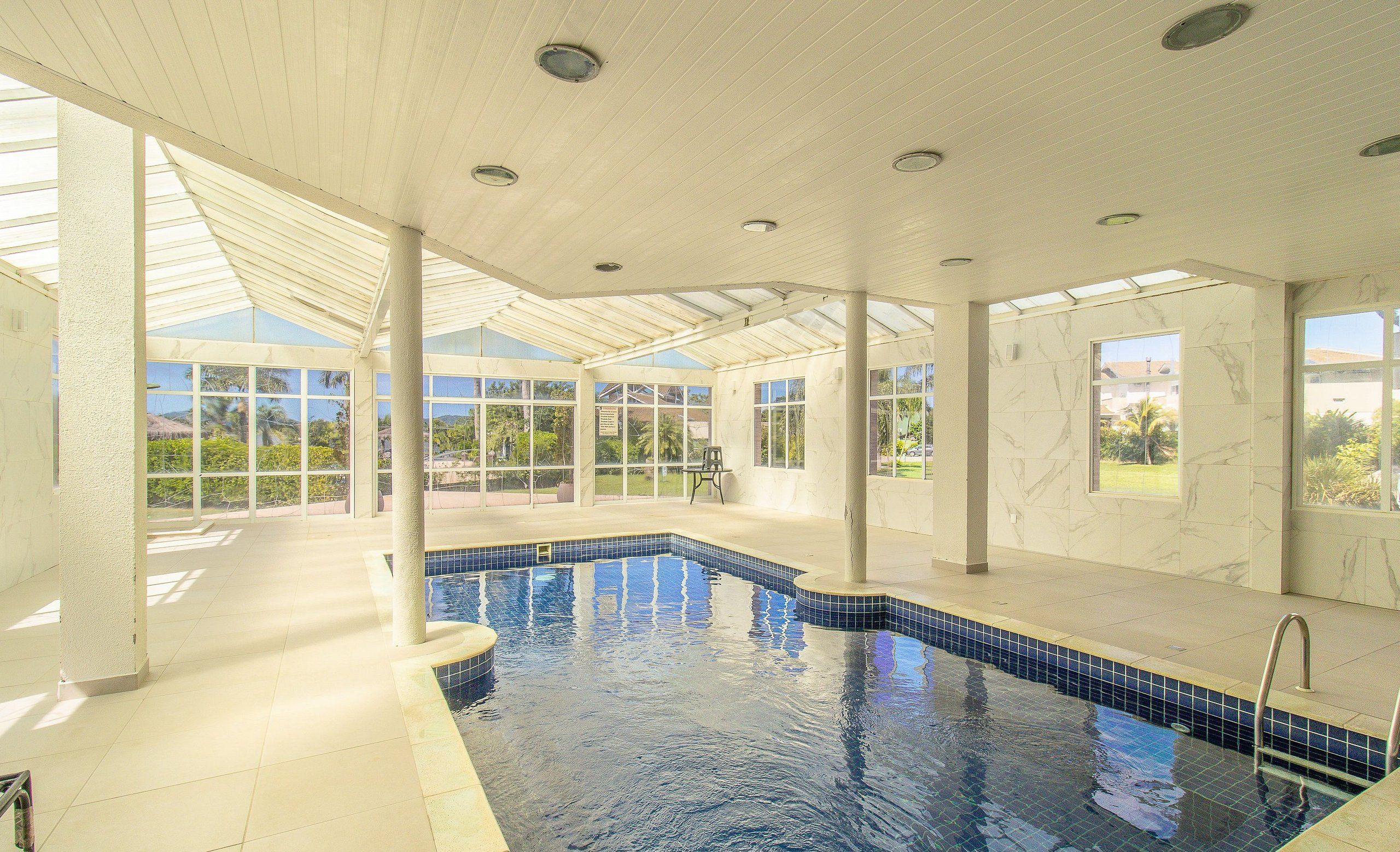 An indoor swimming pool with clear glass walls, a tiled floor, and a ceiling with recessed lighting.