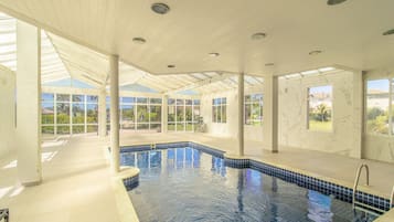 Una piscina interior con paredes de vidrio transparente, suelo de baldosas e iluminación empotrada en el techo.