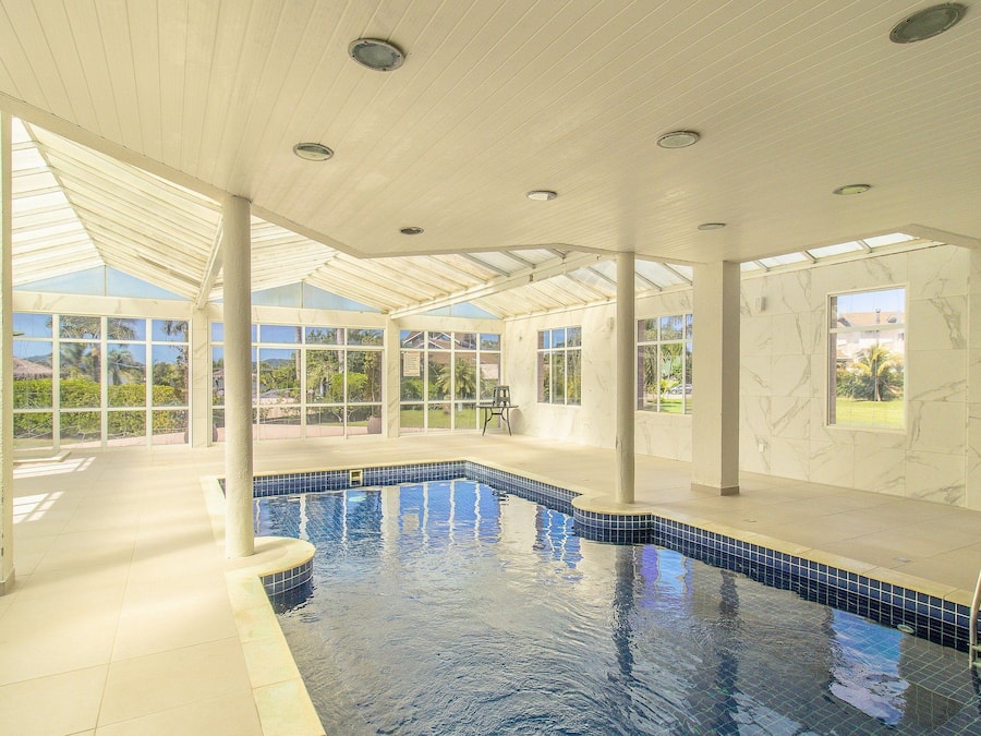 Una piscina interior con paredes de vidrio transparente, suelo de baldosas e iluminación empotrada en el techo.