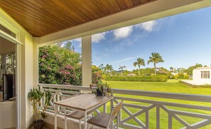 A covered balcony with a wooden table and chairs, a potted plant, and a view of a well-maintained lawn and palm trees. - Apartamento na Lagoa da Conceicao Plg0012 (Florianópolis)