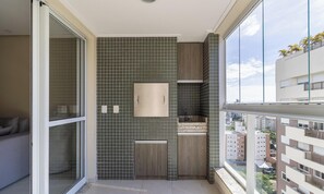 Een moderne badkamer met een betegelde spatwand, een houten wastafelmeubel, een spiegel en een raam met uitzicht op een stadsgezicht.