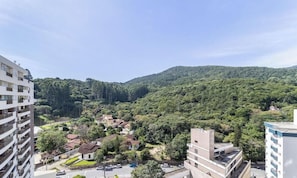Uma área residencial com edifícios, uma estrada e uma colina arborizada ao fundo.